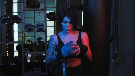 Tattooed pretty woman putting on boxer gloves