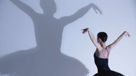 Young woman ballerina in black dress dancing - a big shadow on the wall