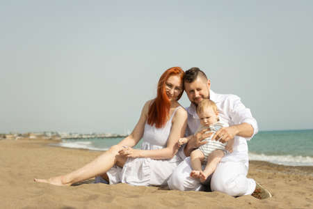 Happy family on vacation sitting on a sand beach with a baby son