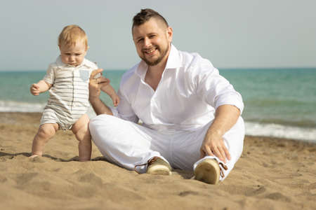 Happy father sitting on a beach with his little sonの写真素材