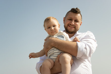 Happy father on vacation - man holding his little baby son on sky background
