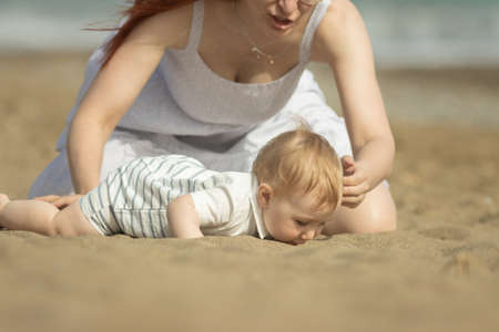 A little boy trying to eat the sand and his mother stopping himの写真素材