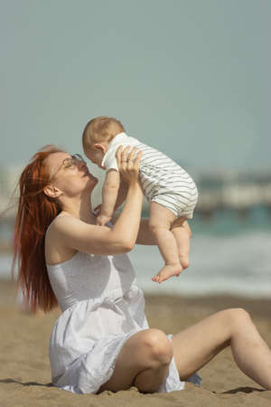 Happy mother and her little son resting on the seaside - raising the baby upの写真素材
