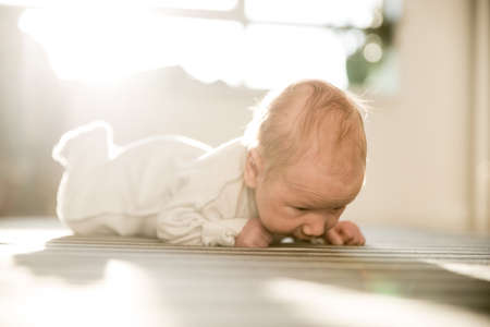 A little newborn baby lying on his stomach on striped sheet and looking down