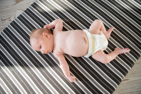 Cute newborn baby in a diaper lying on a bed on striped sheets