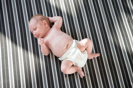 Cute newborn baby in a white diaper lying on striped sheets