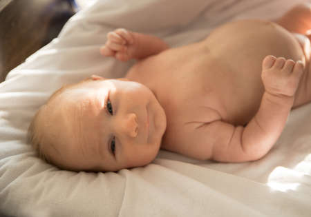 A little baby lying on a bed on white sheets in the sunlight