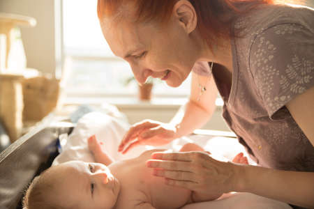 Smiling caring woman playing with her little baby