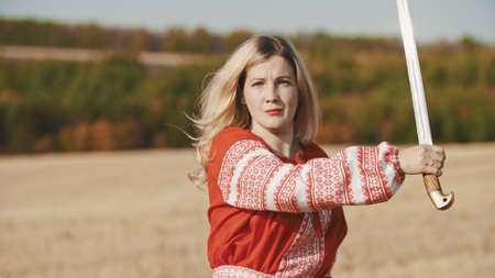 Training in the autumn field - a belligerent woman holding a swordの写真素材