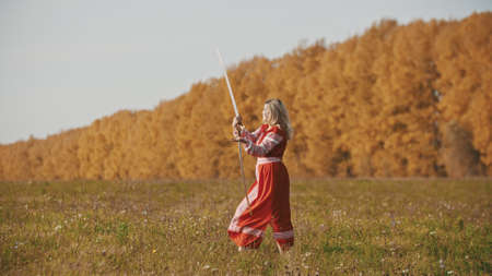 Militant woman in red dress training her swordplay on autumn fieldの写真素材