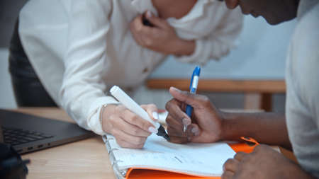 Woman writing something in black mans notebook on english lessonの写真素材