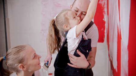 Mom and dad teaching his little daughter how to paint walls - raise her higherの写真素材