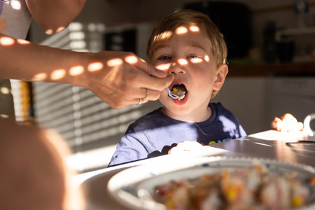 Mom feeds a boy with a spoon in the kitchenの写真素材