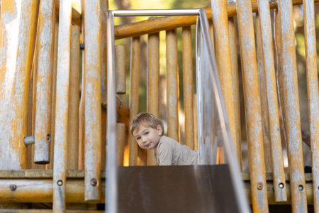 Funny little boy on playground - looking in the camera from the building with a slideの写真素材