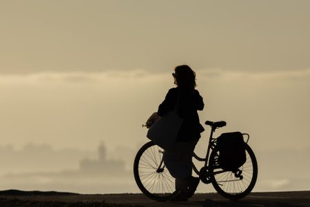 Silhouette of a woman with a bicycle at sunsetの写真素材