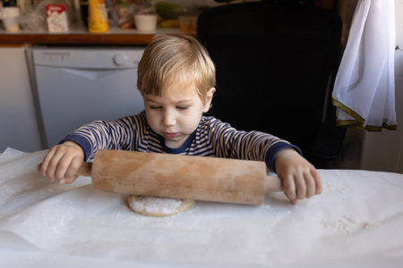 Family cooking - a little boy works with a rolling pin with raw doughの写真素材