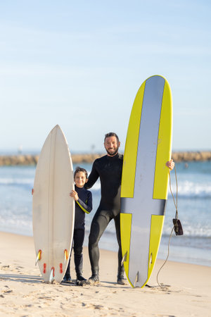 A family of surfers - father and son standing on the seashore with their surfing boardsの写真素材