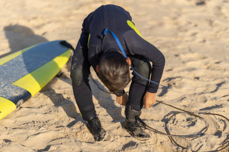 A man surfer fastens a board to his leg while sitting on the shoreの写真素材
