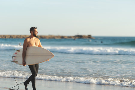 A smiling man surfer with naked torso walking on the seashoreの写真素材