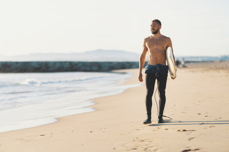An athletic man surfer with naked torso standing on the seashoreの写真素材