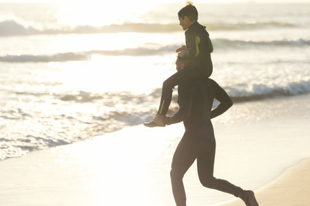 Little son on the shoulders of his father running to the sea at sunsetの写真素材
