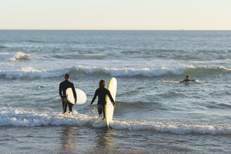 A man and a woman go out to sea holding surfboardsの写真素材