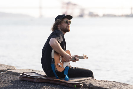A man hipster playing electric guitar at the waterfront