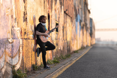 Romantic man hipster wearing sunglasses standing by the wall playing electric guitar at early sunsetの写真素材