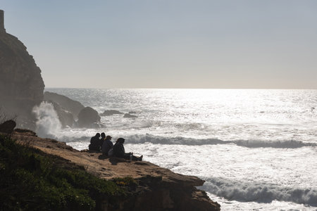 People sit on rocks and look at the sea wavesの写真素材