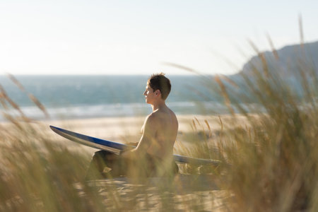 A man sitting on the beach holding a blue surfboardの写真素材