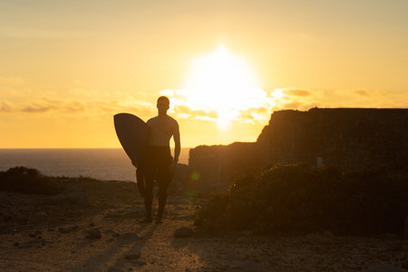 Fit man with naked torso standing nearby ocean at bright sunsetの写真素材