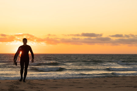 Silhouette of a man in wetsuit walking forward at bright orange sunsetの写真素材