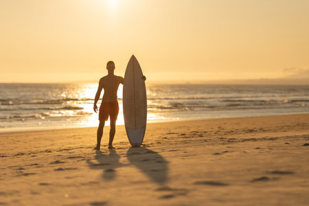 Silhouette of a man standing on the shore holding a surfboardの写真素材