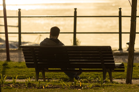 Lonely man sitting on a bench at early sunsetの写真素材