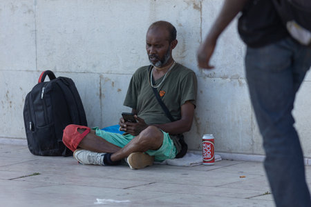 Photo for Lisbon, Portugal - 24 june 2023: black man sits on the blanket on the sidewalk and looking at his phone - Royalty Free Image