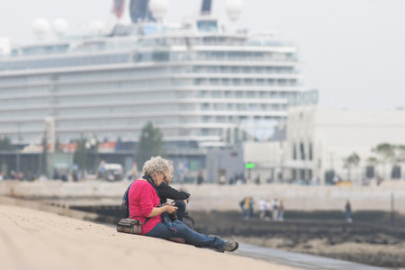 29 october 2022 Lisbon, Portugal: an old couple sitting on the beach with a huge cruise liner on the backgroundのeditorial素材