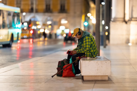 27 July 2023 Lisbon, Portugal: Old man in headphones reading a book on the streetのeditorial素材