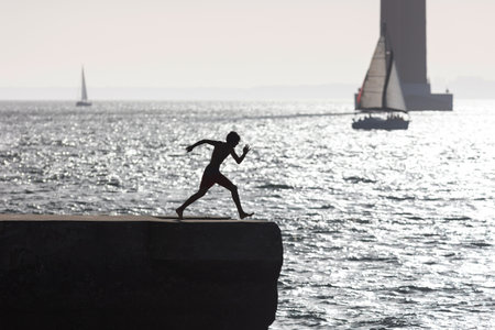 A boy in swimming trunks scatters on the pier before jumping into the water - monochrome imageの写真素材
