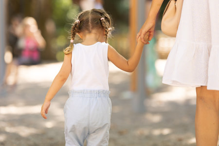 A little girl walking in the park holding her mother by hand - view from the backの写真素材