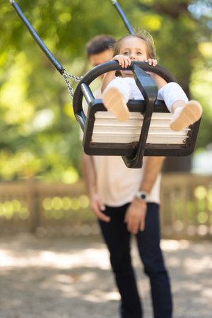 Daughters father rides his daughter on a swing in a summer parkの写真素材
