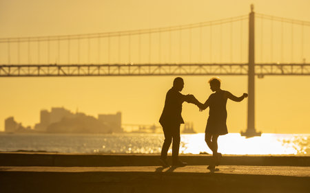 Silhouettes of dancing elderly couple holding hands during sunset