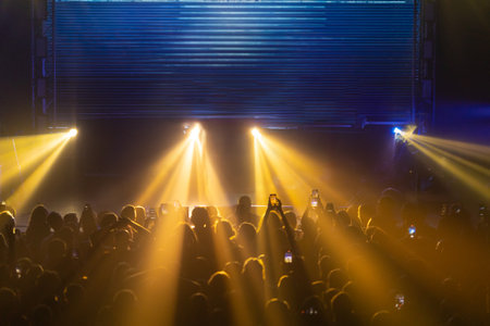 Stage lights creating a dramatic concert atmosphere - a lot of people with phone looking to shoe and waitingの写真素材
