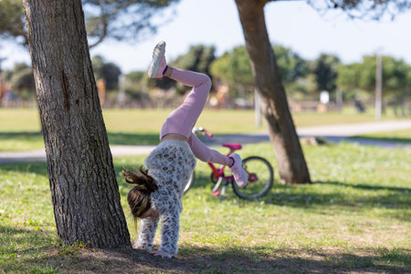 A girl is doing a handstand on a tree trunk in a park