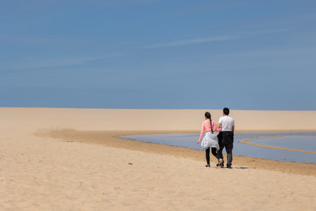 A couple walking on a beach with a clear blue sky above themの写真素材