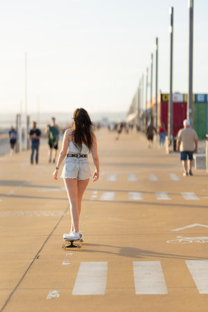 A woman is skateboarding down a sidewalkの写真素材