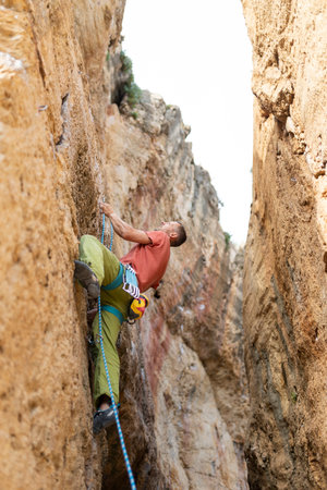 A man is climbing a rock wall with a blue rope