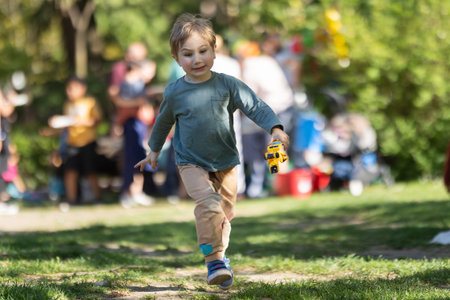 A young boy is running through a park with a toy bus in his hand