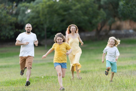 Happy family running through grass in the parkの写真素材