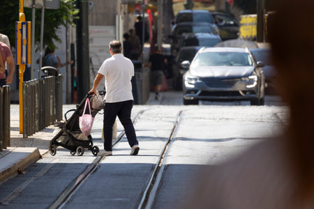 Father pushing stroller crossing tram tracks in urban settingの写真素材