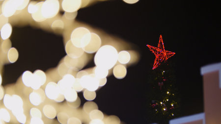 Christmas tree with red star is shining on background of blurred christmas lightsの写真素材